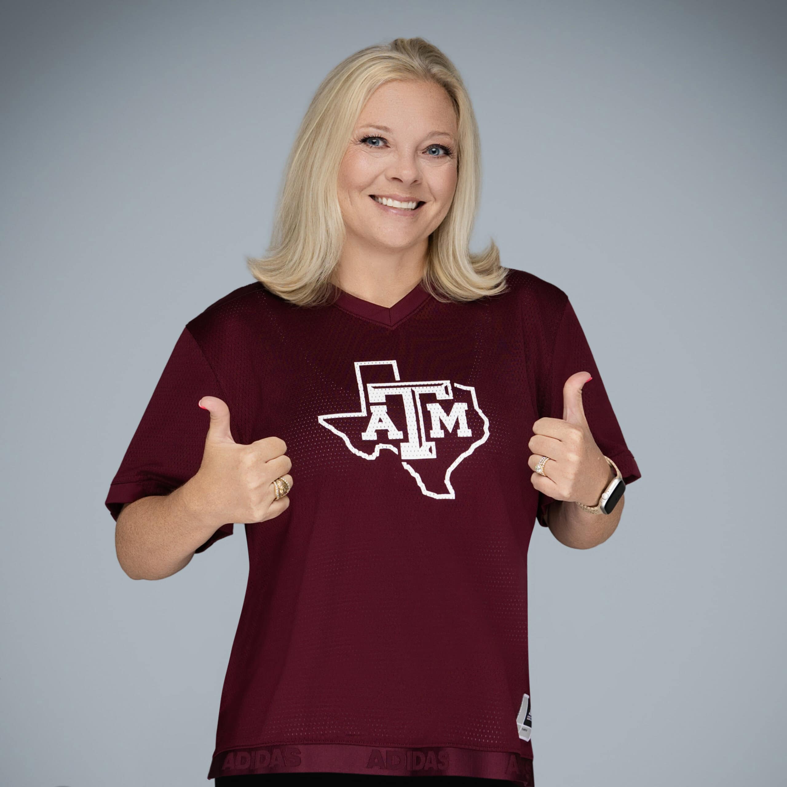 Woman in Texas A&M shirt giving thumbs up for community and education.