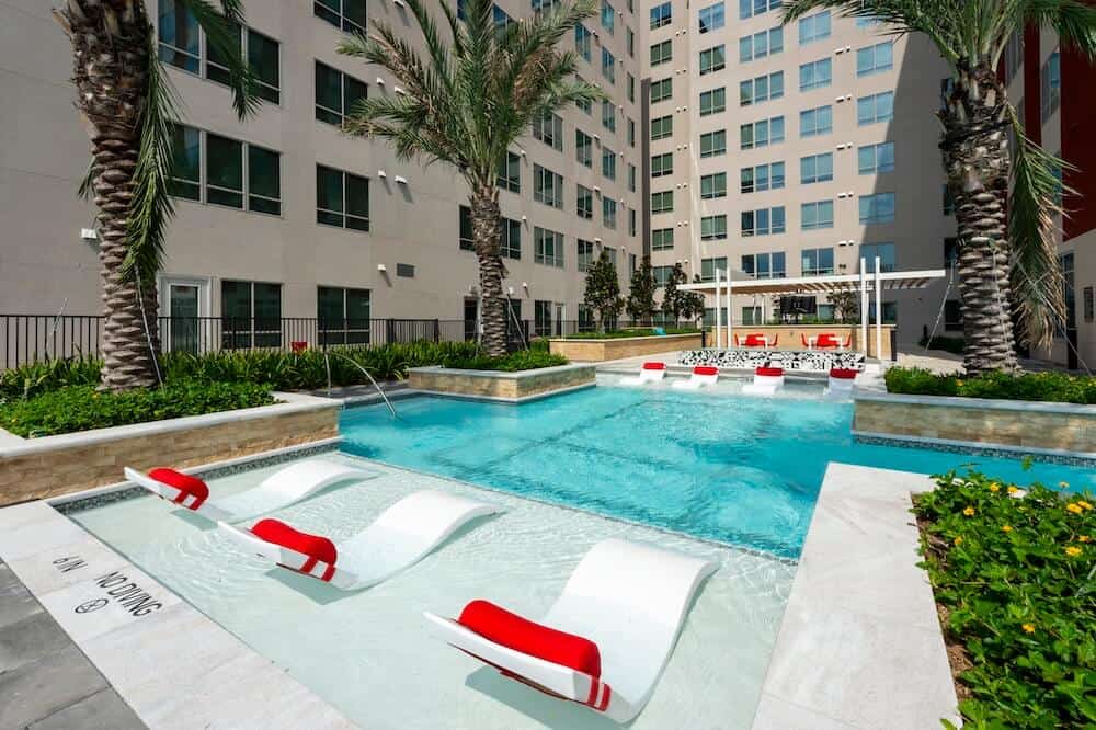 Modern apartment complex pool with lounge chairs and palm trees.